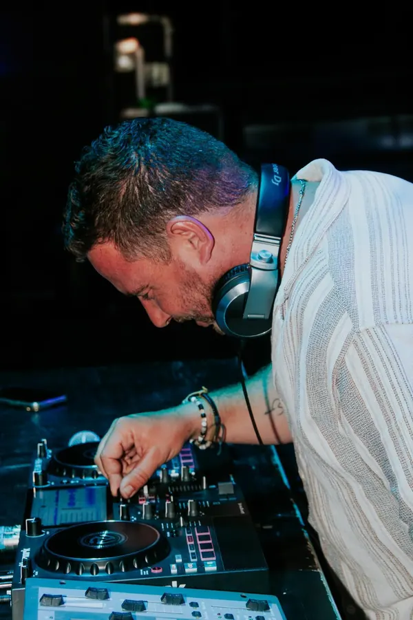 Camolas DJ de perfil, com auscultadores, a ajustar o controlador